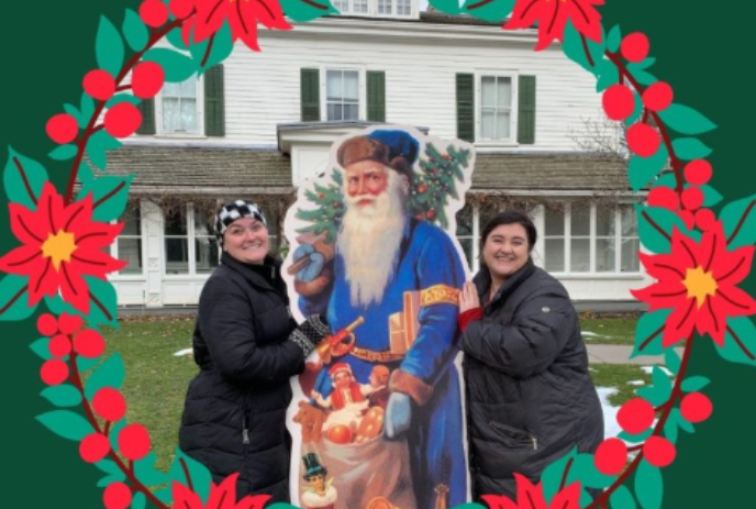 Two people standing beside a cardboard cutout of a Father Christmas with a bag of toys.
