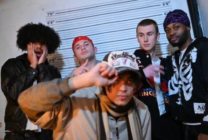 Five artists posing for a pictures under a white background with horizontal black lines.