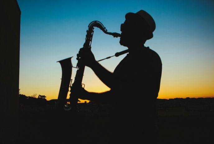 Silhouette of a saxophonist in a hat playing at sunset, with a vivid blue and orange sky.