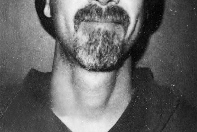 Artist in grainy black-and-white with the lower face, wearing a beanie, with a dark background.
