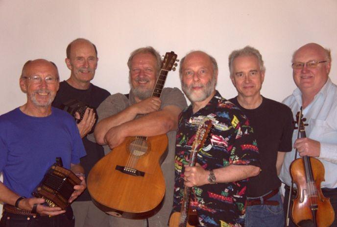 Six smiling artists with instruments pose together, suggesting a joyful folk band in a casual setting.