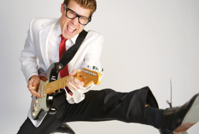 Person wearing a white sport coat, playing guitar and dancing.