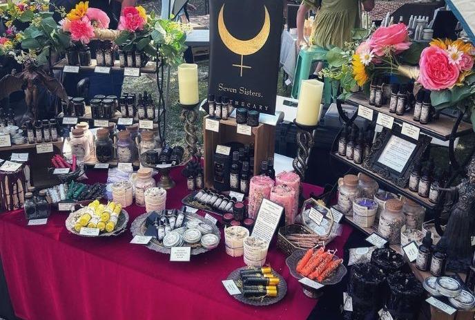 Apothecary stall with herbal goods, candles, and mystical decor under 'Seven Sisters' sign.
