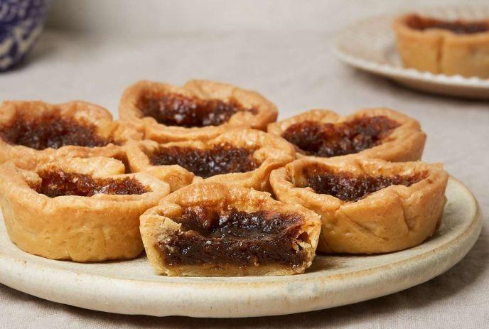 Butter tarts with flaky crust and filling sit on plates with a white background.