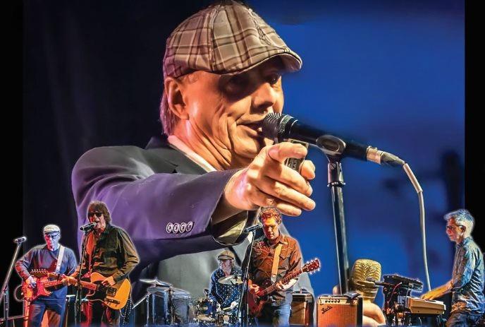 Singer in flat cap points at camera withChuck Jackson live band playing guitars, drums, and keyboard.