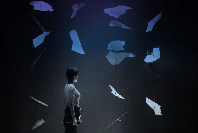 Person stands in front of paper images floating in a pattern.