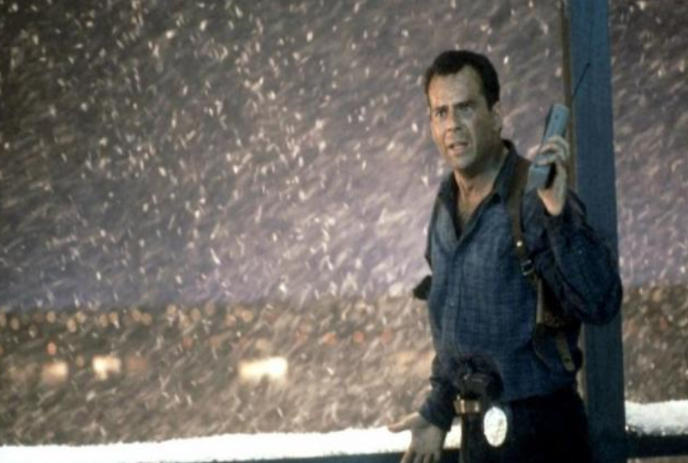 John McClane holding a phone in a snowy scene.