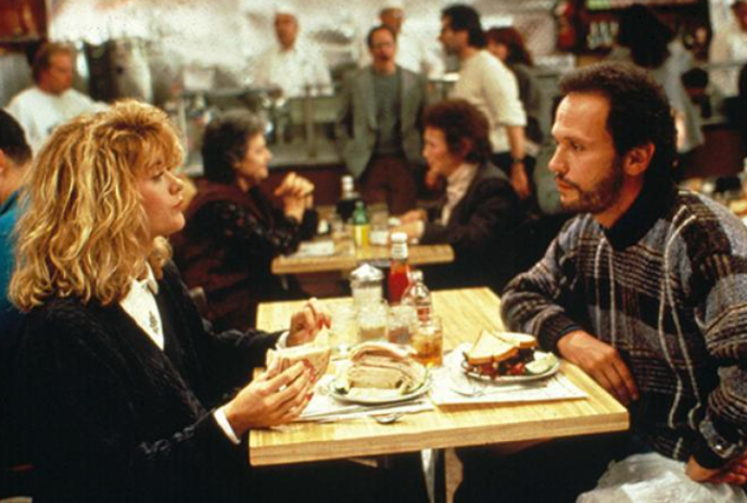 A man and a woman sit at a table in a busy diner, staring at each other