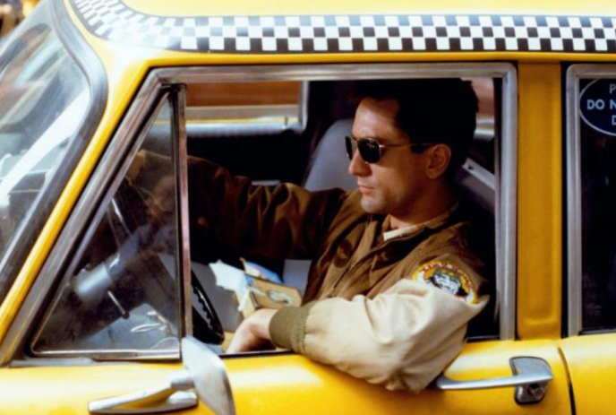 Person wearing sunglasses sits in the driver's seat of a yellow taxi.