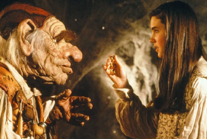 A young person stands in front of a Goblin while holding a bracelet out.
