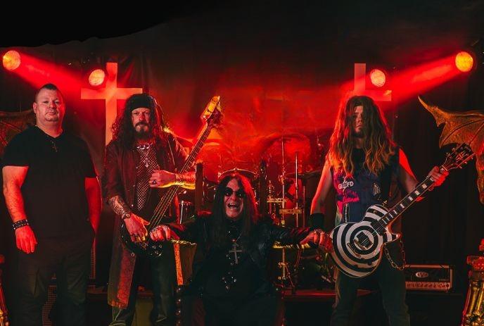 Rock band posing onstage in red light, four members with guitars and dramatic stage props.