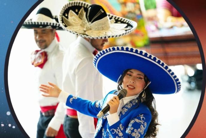 Singer in blue mariachi suit performs with two musicians in sombreros at a festive cultural event.