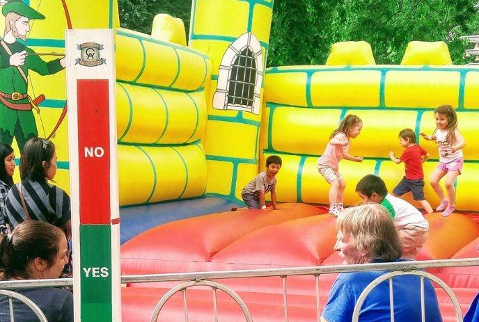 Children play and bounce inside a yellow inflatable castle while adults watch from behind a metal barrier.