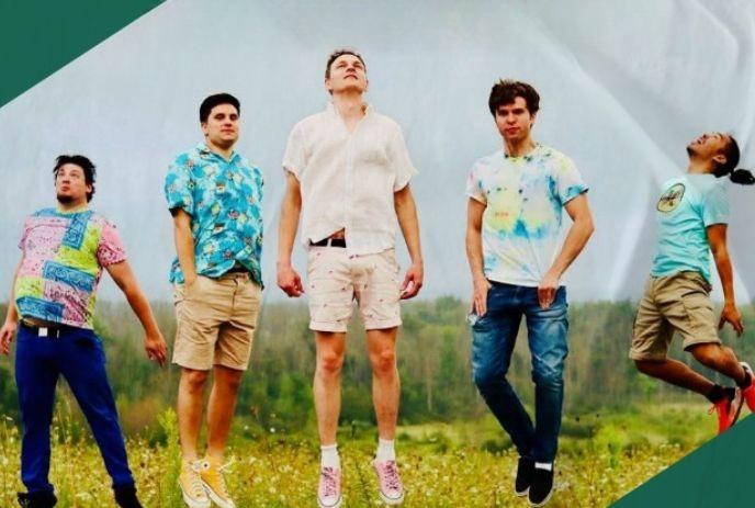 Five artists jumping in a grassy field, wearing bright summer clothes before a forest background outdoorsy