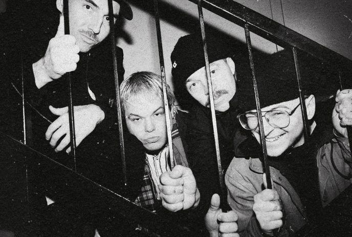 Four artists behind metal bars in a black and white frame.