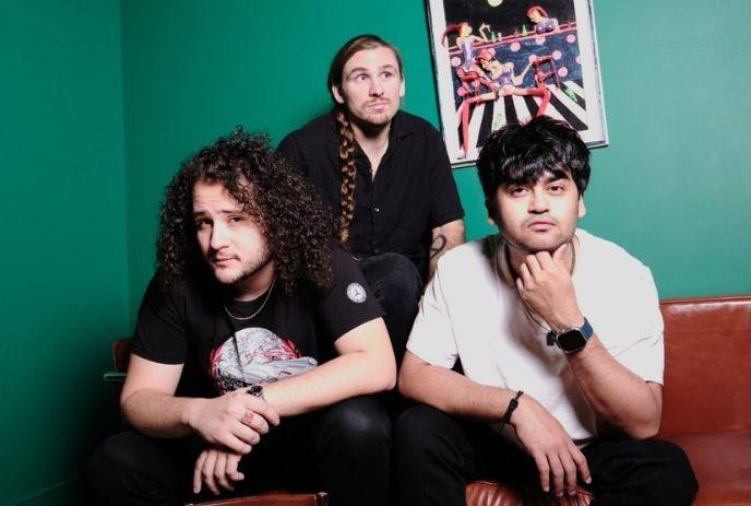 Three artists sitting on a couch against a green wall with framed boxing art in the background.