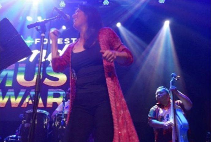 singer in red performing onstage with bassist behind her under bright colorful lights.