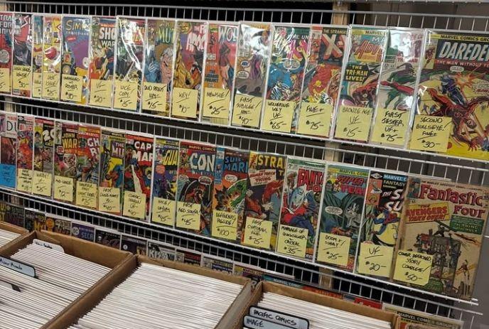 Comic books in sleeves line racks with price tags and boxes below labeled by publisher.