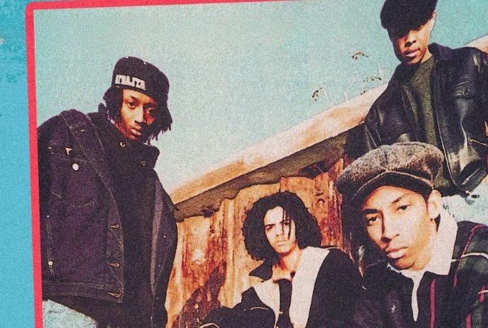 Four artists in casual streetwear pose outdoors before wooden structure under clear sky with relaxed energy.