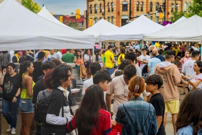 Crowded street market with white tents and people walking, browsing, and enjoying a sunny day.