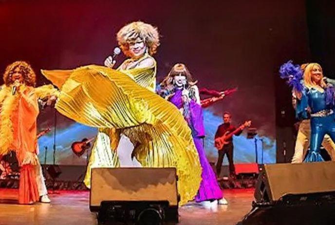 Performers in bright retro costumes sing and dance on stage with musicians under warm colorful lights.