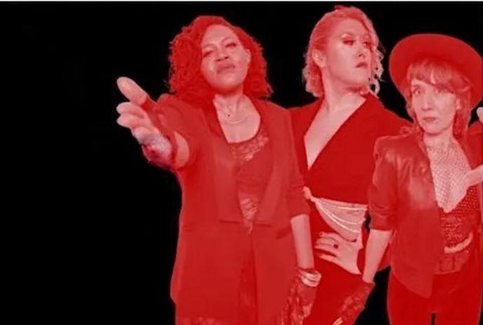 Three stylish artists in red tint pose against black backdrop with bold outfits.