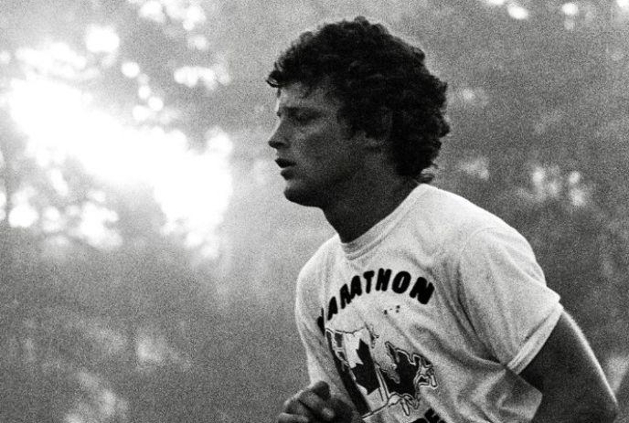 Terry Fox running in misty light wearing a marathon shirt, moving through trees in a dramatic black?and?white scene