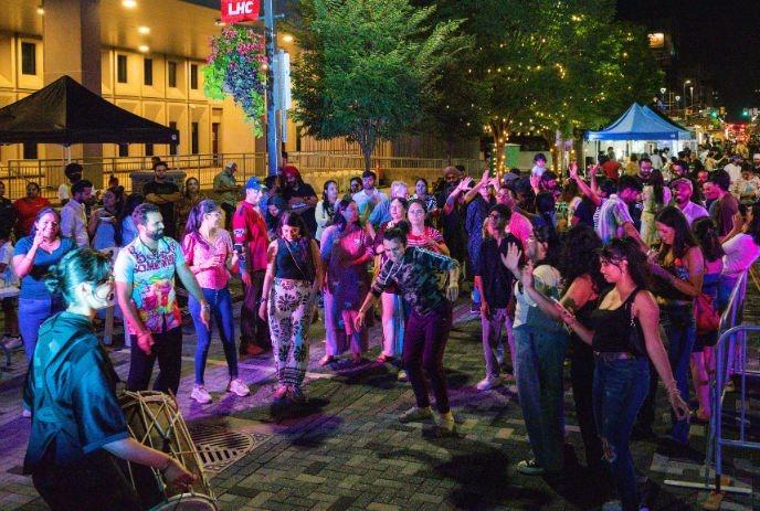 Night street festival with a drummer leading a lively crowd dancing under colorful lights.