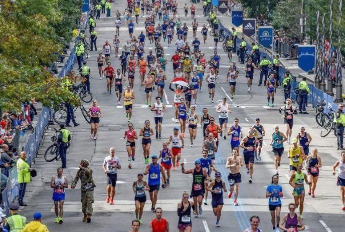 Crowded city marathon with diverse runners on wide street, spectators and police lining the route.