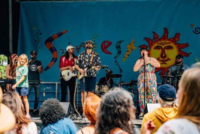 Musicians at the Sunfest stage; vibrant banner and cheering crowd radiate daytime festival joy.