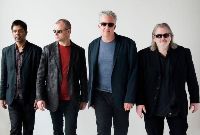 Four artists in dark attire and sunglasses pose confidently against a white backdrop.