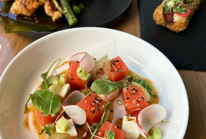 Colorful plated watermelon cubes with radish, avocado, cheese, and microgreens on a bright dish.