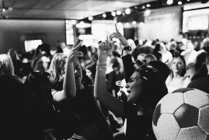 Black?and?white crowd dancing with raised hands, a large soccer?ball graphic overlaying the scene.