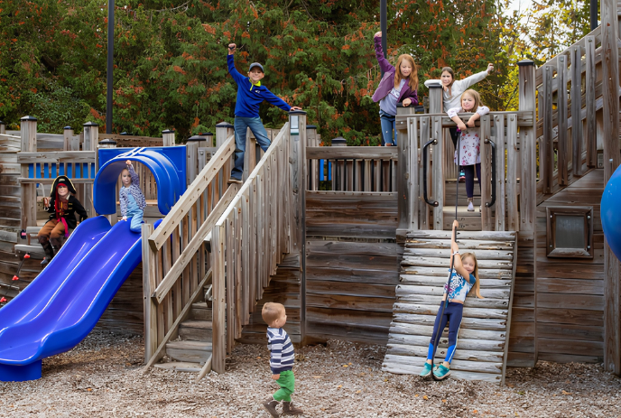 Children playing together on a  wooden playground with blue slides.