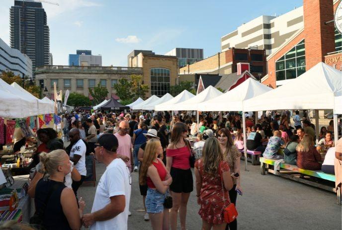 A crowd of people attending festival at Covent Garden Market with various vendors with white canopy tent under a sunny day.
