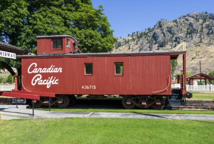 Red Canadian Pacific Caboose sits in front of a green tree and a large hill.