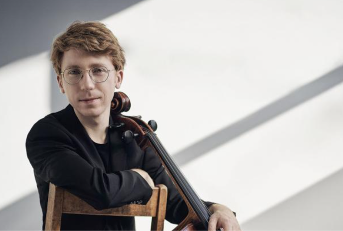 Cellist Cameron Crozman sits on a chair with his cello.