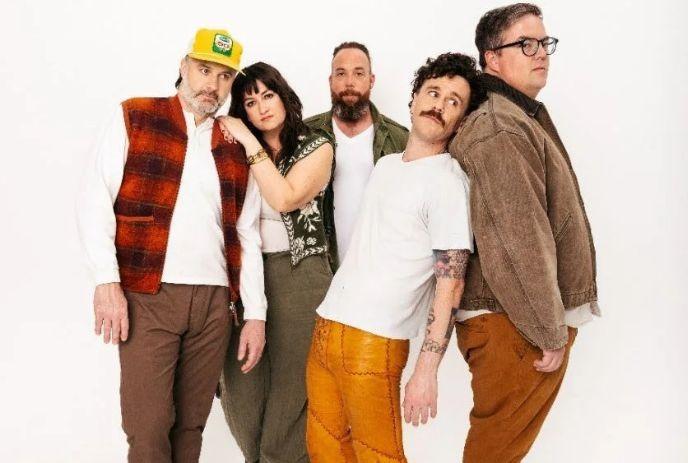 Five band members from the strumbellas posing together against white backdrop wearing varied casual outfits.
