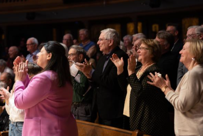 A group of people stand together while clapping.