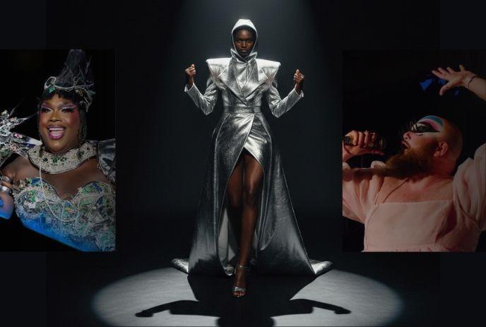 Models in reflective silver outfits under spotlight with sharp shoulders hood high slit posing in dark setting.