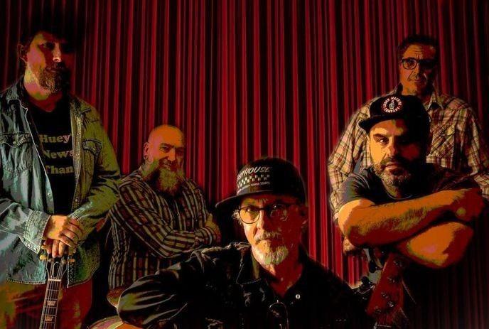 Five artists pose before red curtains with warm dramatic lighting highlighting guitars clothing and expressive mood