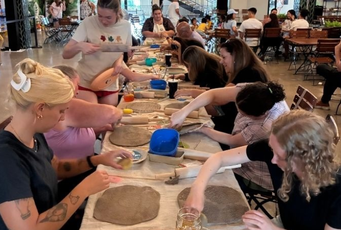 Group of people sitting at a long table working with clay in front of them.