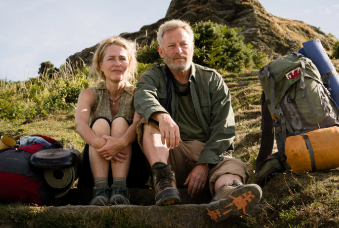 Two middle-aged people sit together on a rugged mountain with their gear.