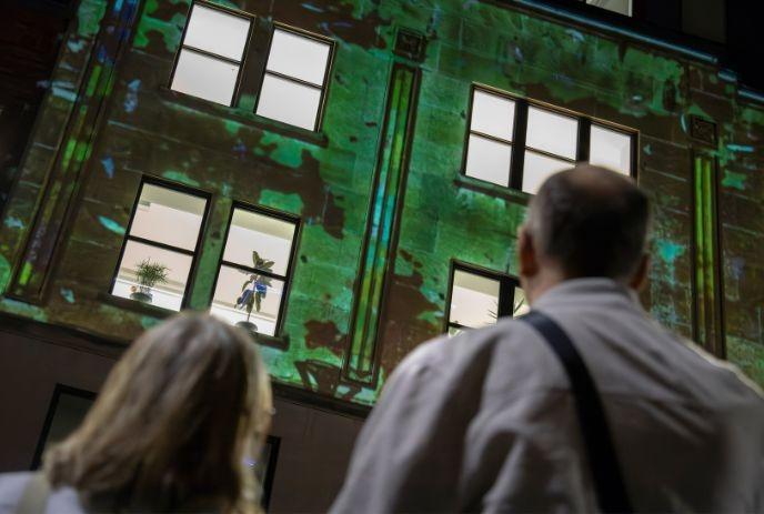 People viewing a green light projection displayed across the windows and facade of a building.