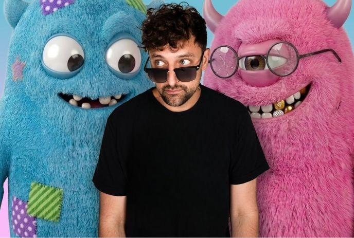 Artist in black shirt and sunglasses stands between blue and pink fuzzy cartoon monsters smiling.