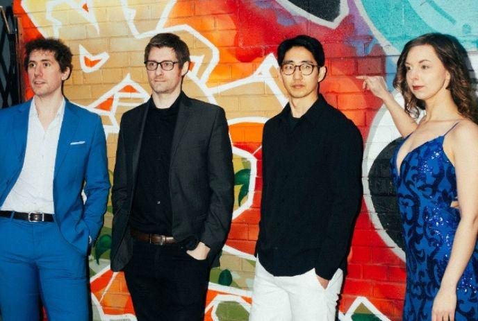 Four artists posing in formal attire before a colorful graffiti mural, with vibrant red, blue, and teal tones.