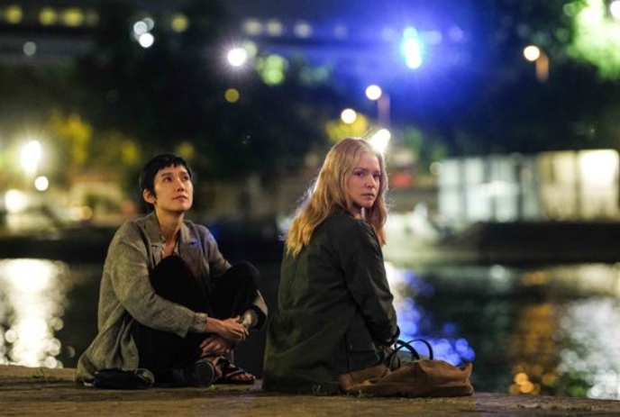 Two people sit together by the waterfront in the evening.