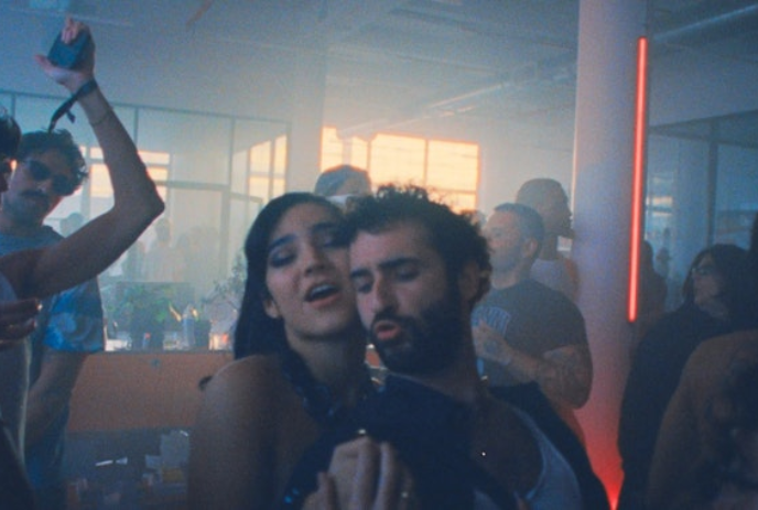 Two people dancing close inside a night club while others dance around them.