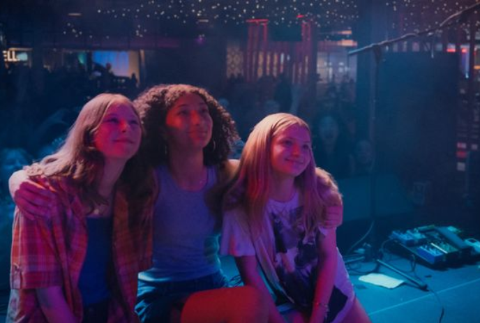 Three teenage friends stand together looking at something off-screen.