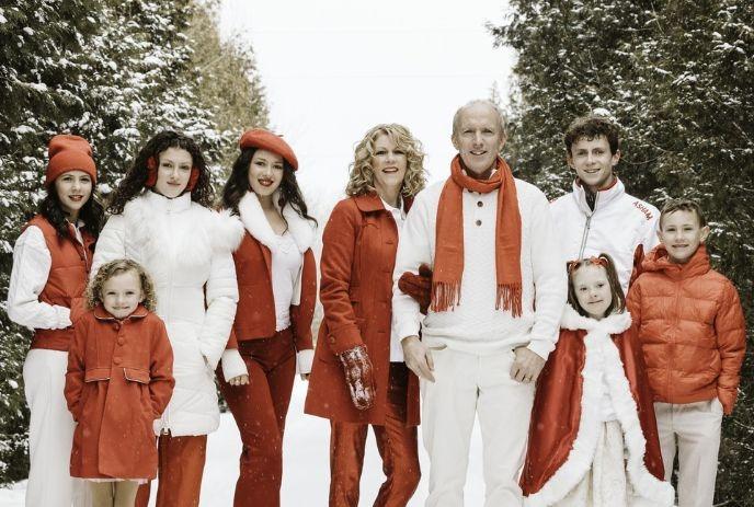 Snowy path family portrait in red and white winter outfits among greens creating a festive seasonal scene.